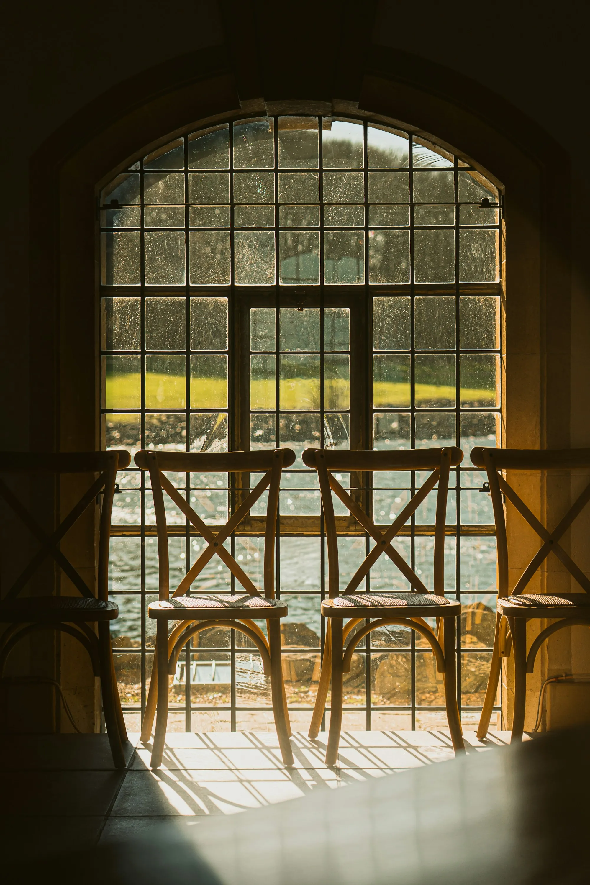 A pair of wooden chairs facing a tall arched window, sunlight falling across the floor